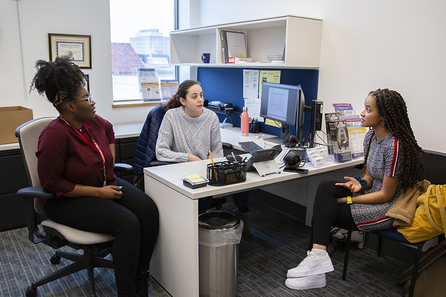Three graduate students have a discussion in the public policy main office.