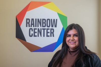 Photo of Brianna Vig in front of Rainbow Center Logo